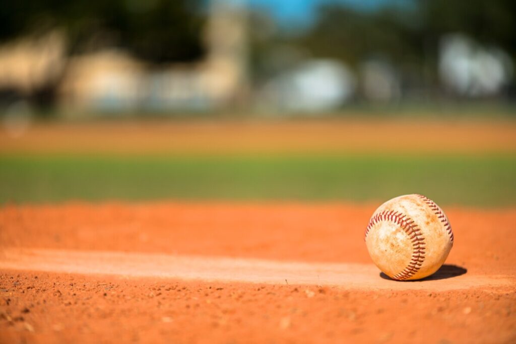 A baseball sits on the ground of a baseball diamond.